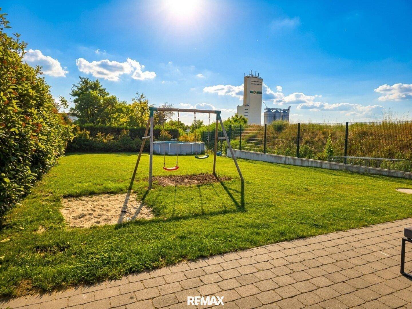Grüner Garten mit Schaukel, Sandkasten und einem kleinen Pool im Hintergrund.