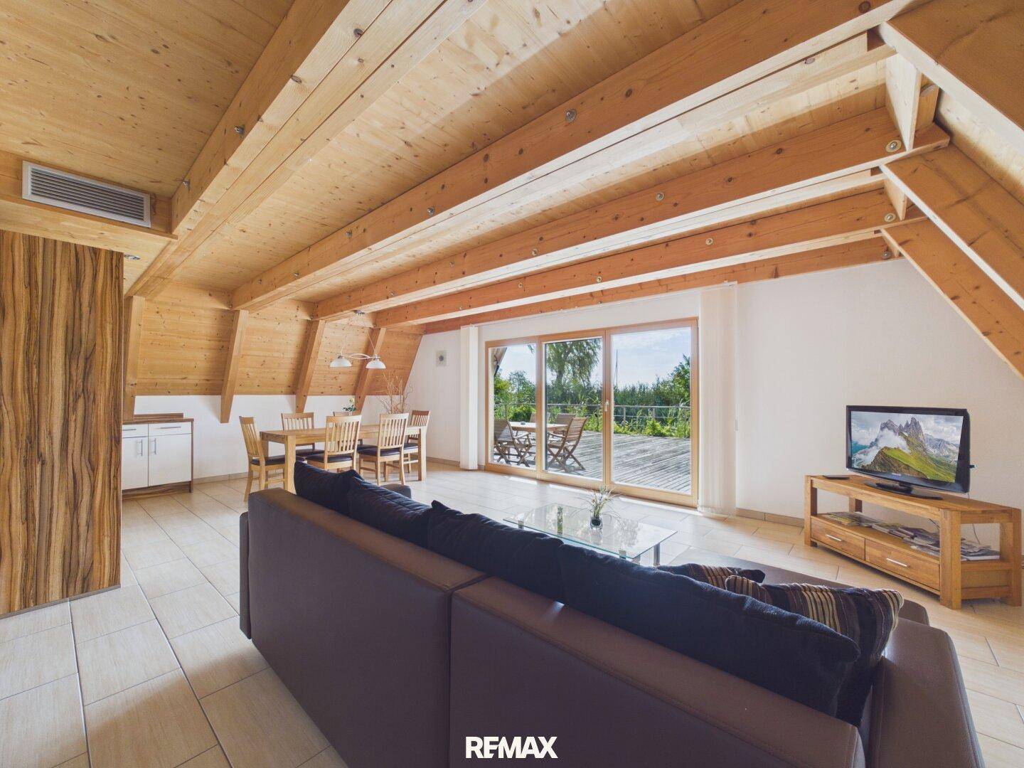 Heller Wohn- und Essbereich mit Holzbalkendecke, Fliesenboden und Zugang zu einer großen Terrasse.