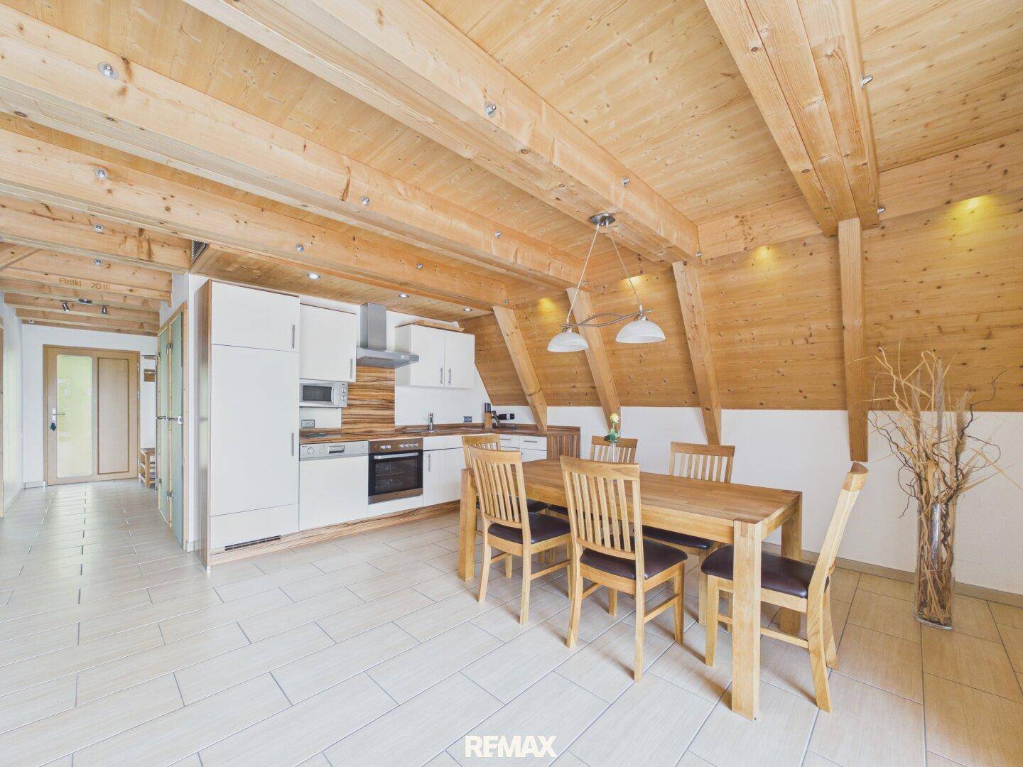 Moderne Einbauküche mit weißen Schränken, Holzbalkendecke und Essbereich.