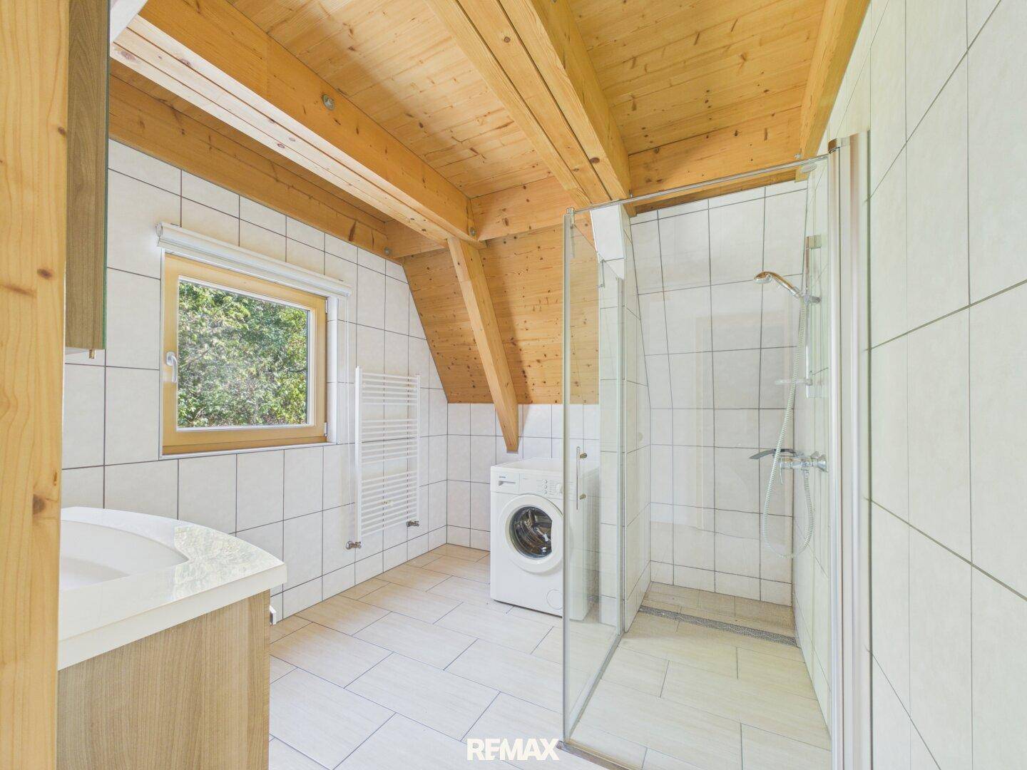 Modernes Badezimmer mit Dusche, Waschmaschine und Fenster, unter einer Dachschräge.