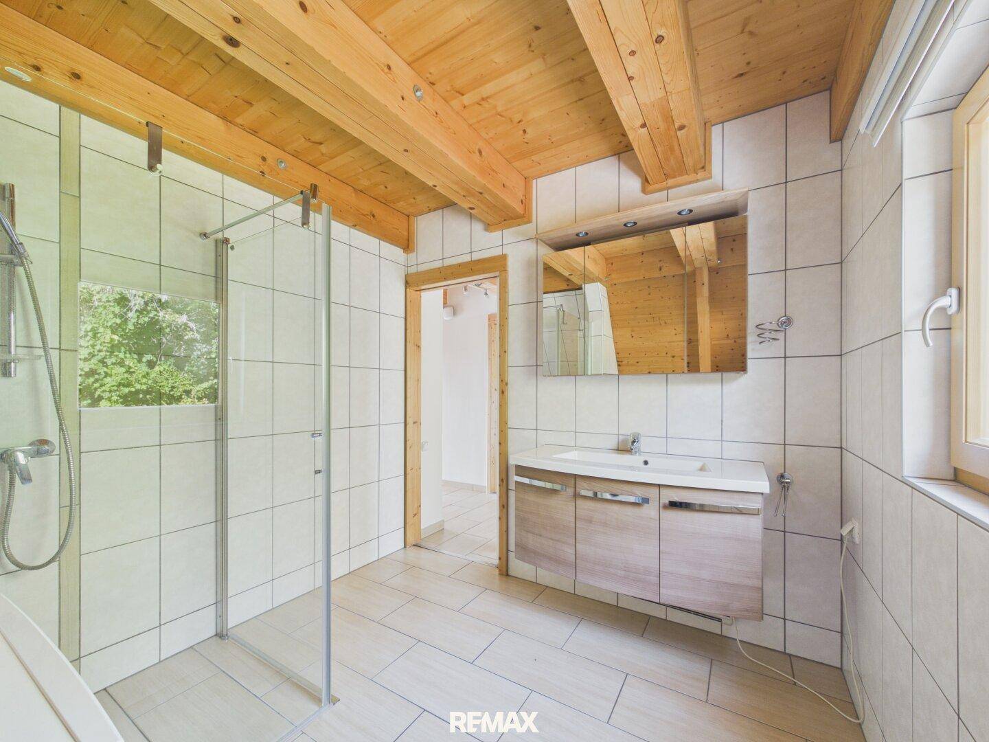 Helles Badezimmer mit Dusche, Waschtisch und Spiegel, unter einer Dachschräge.