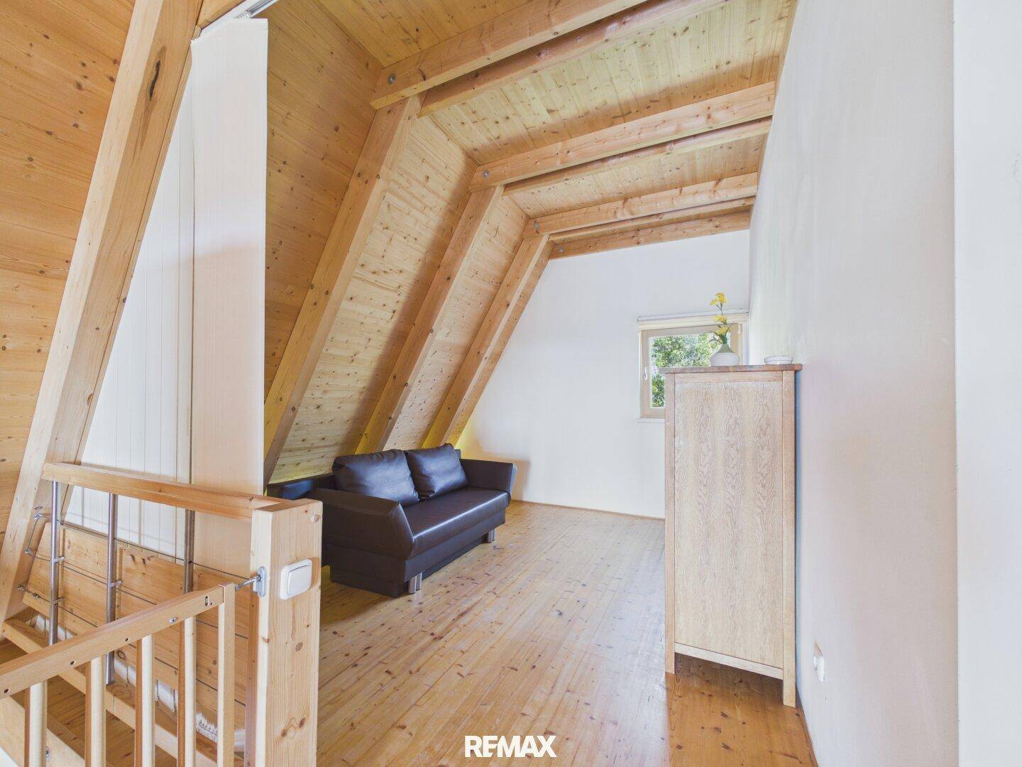 Offener Wohnbereich im Obergeschoss mit Holzboden, Holzbalkendecke und Sofa.