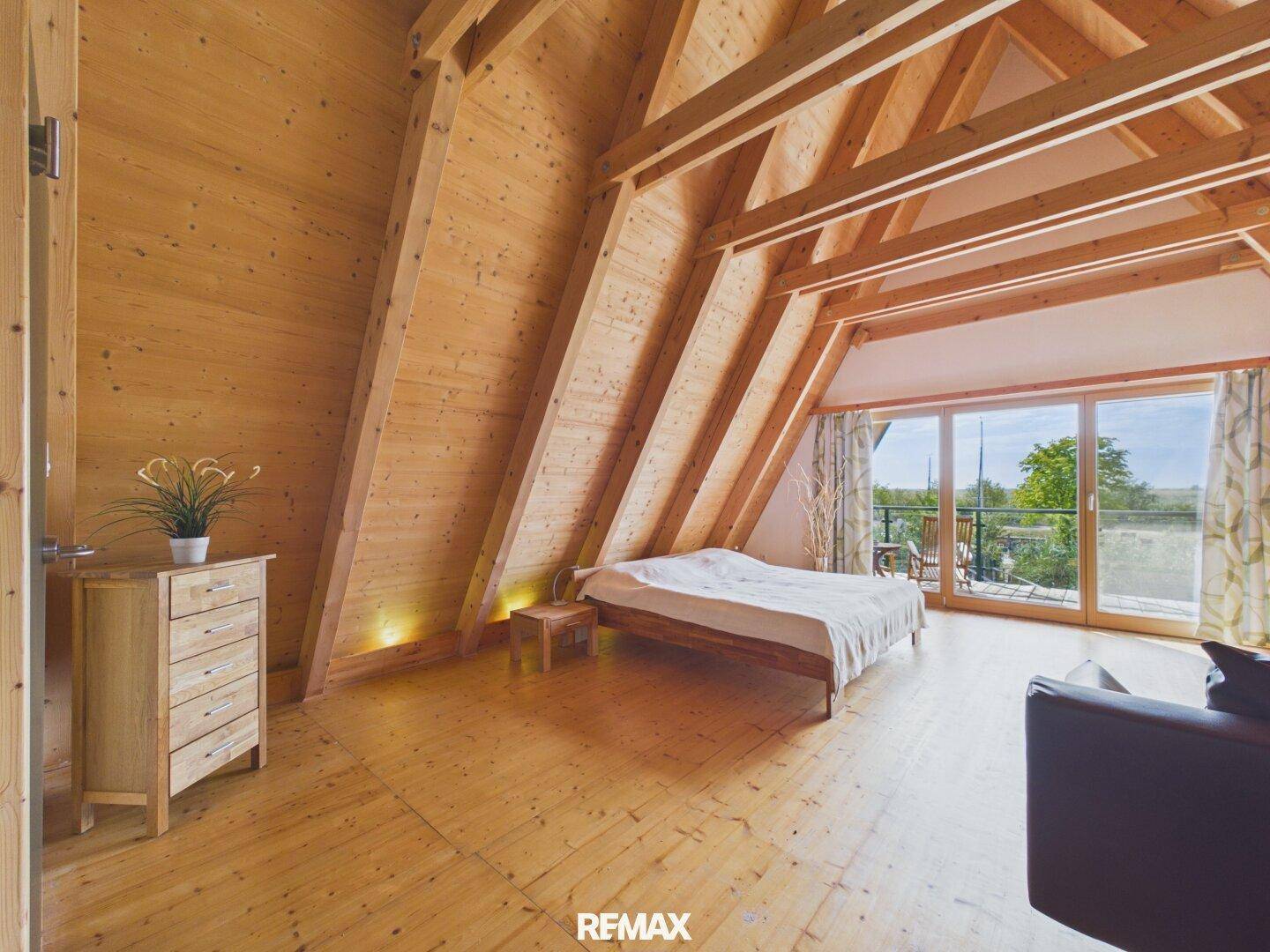 Geräumiges Schlafzimmer mit Holzboden, Holzbalkendecke und direktem Zugang zum Balkon.