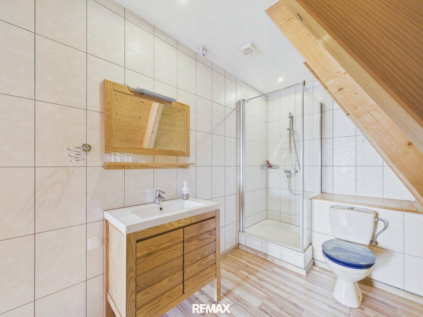 Badezimmer mit Dusche, WC und Waschtisch, unter einer Dachschräge.