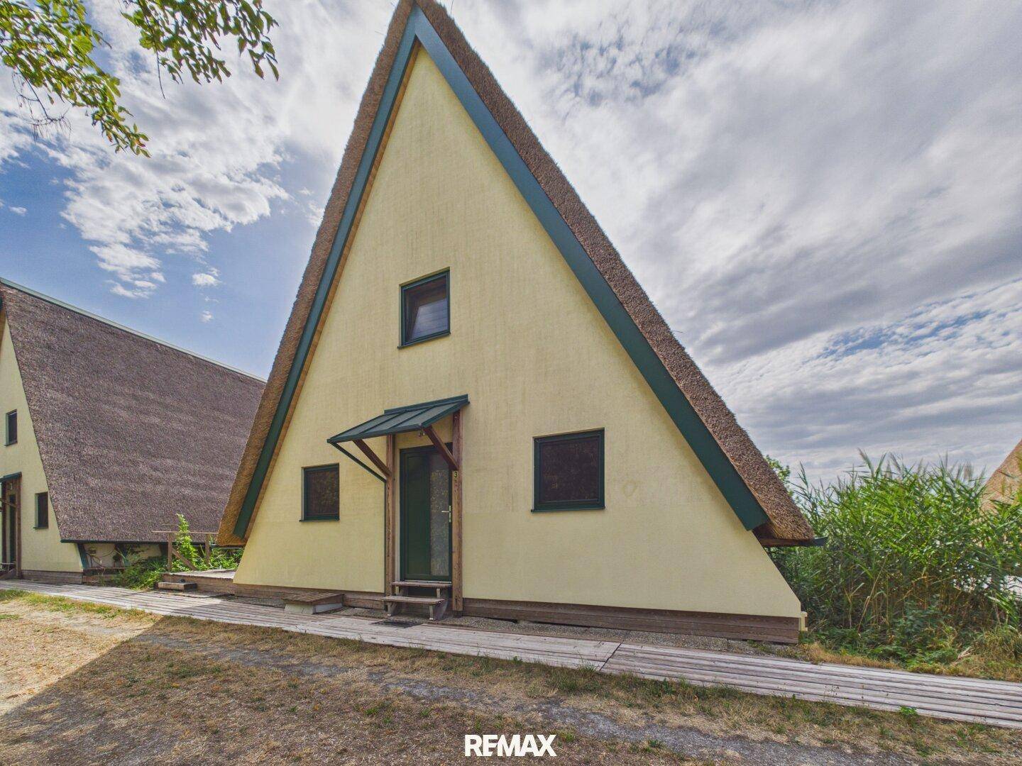 Vorderansicht eines A-förmigen Hauses mit Reetdach und gelber Fassade.