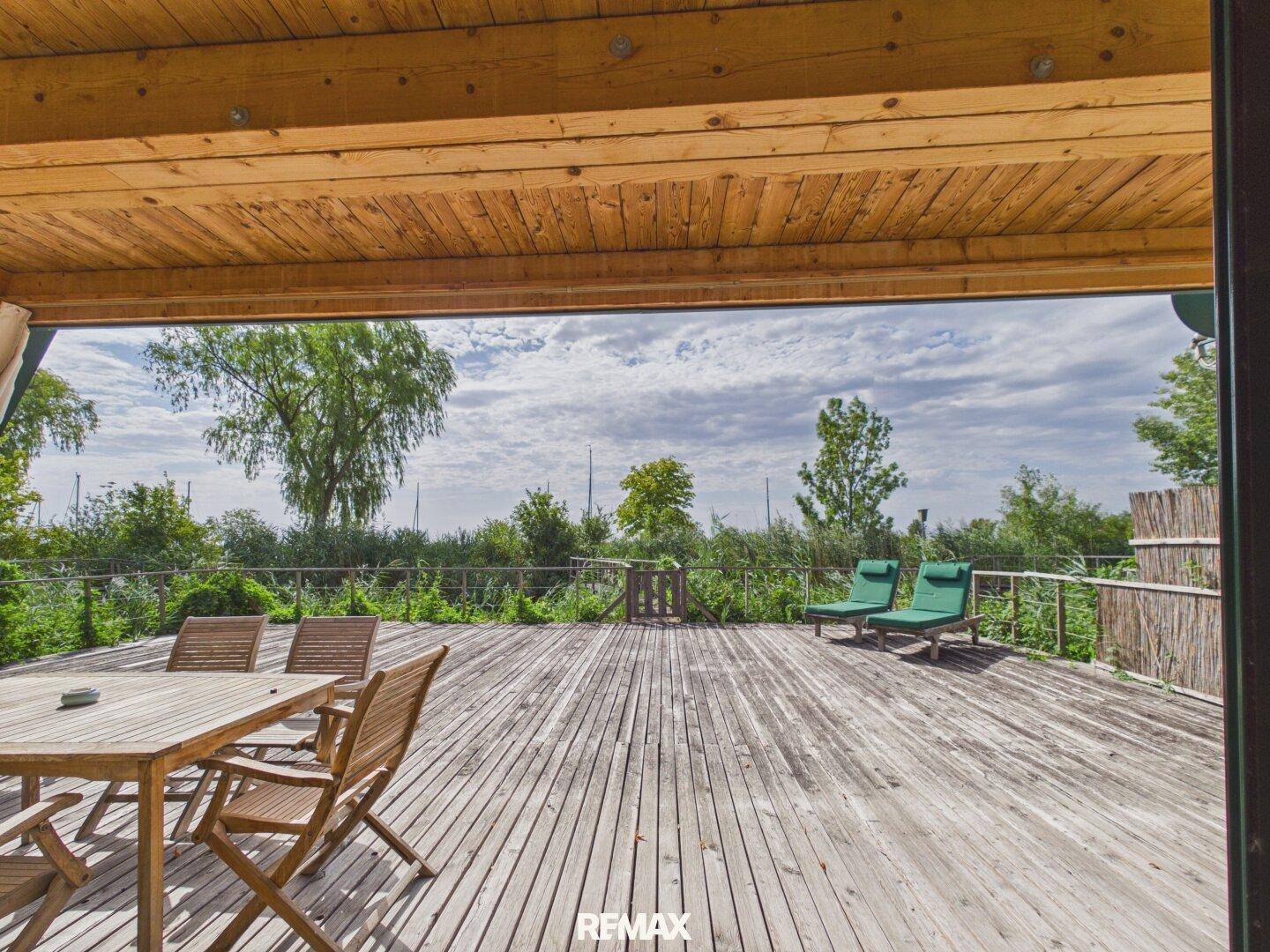 Geräumige Holzterrasse mit Sonnenliegen und Esstisch, umgeben von üppiger Natur.