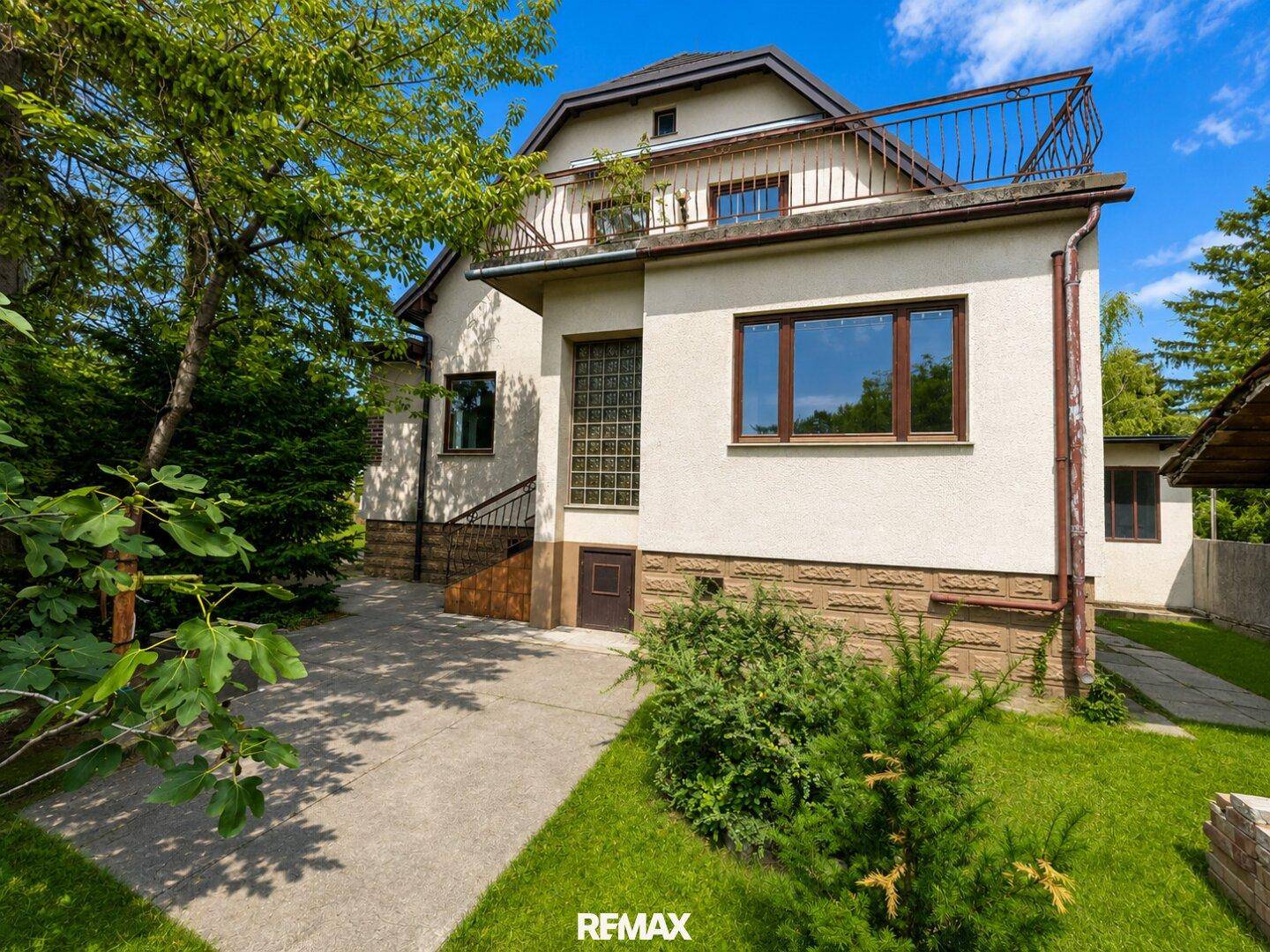 Seitenansicht des Hauses mit Zugang zum oberen Balkon und einem gepflasterten Weg im Grünen.