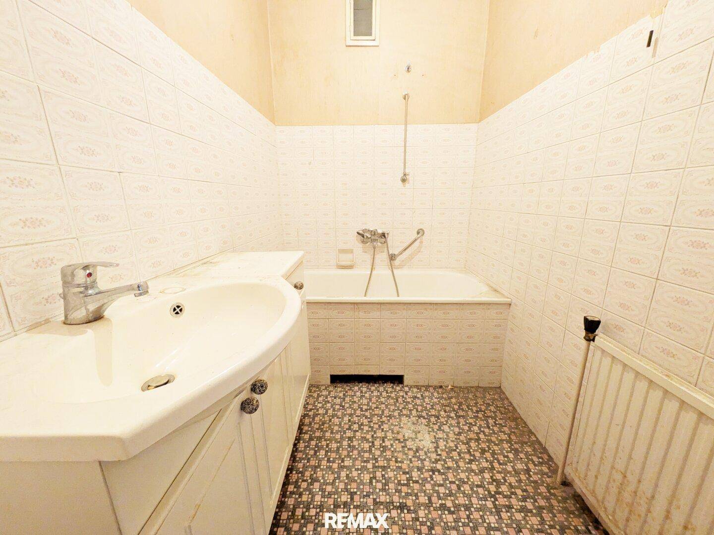 Badezimmer mit Badewanne, Waschbecken und gemusterten Fliesen, das eine Modernisierung benötigt.
