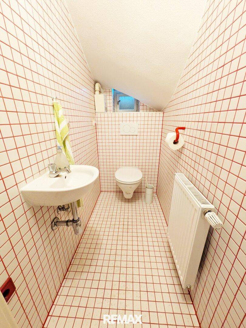 Kleines Gäste-WC mit roten Fliesen, Waschbecken und Toilette unter einer Dachschräge.