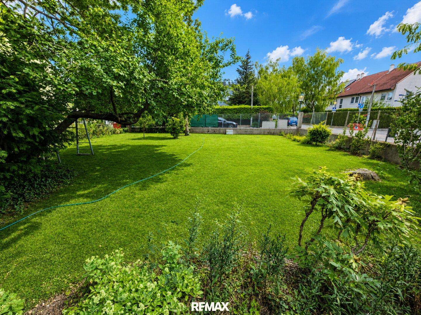 Großer, gepflegter Garten mit weitläufigem Rasen, alten Bäumen und Blick auf die Nachbarschaft.