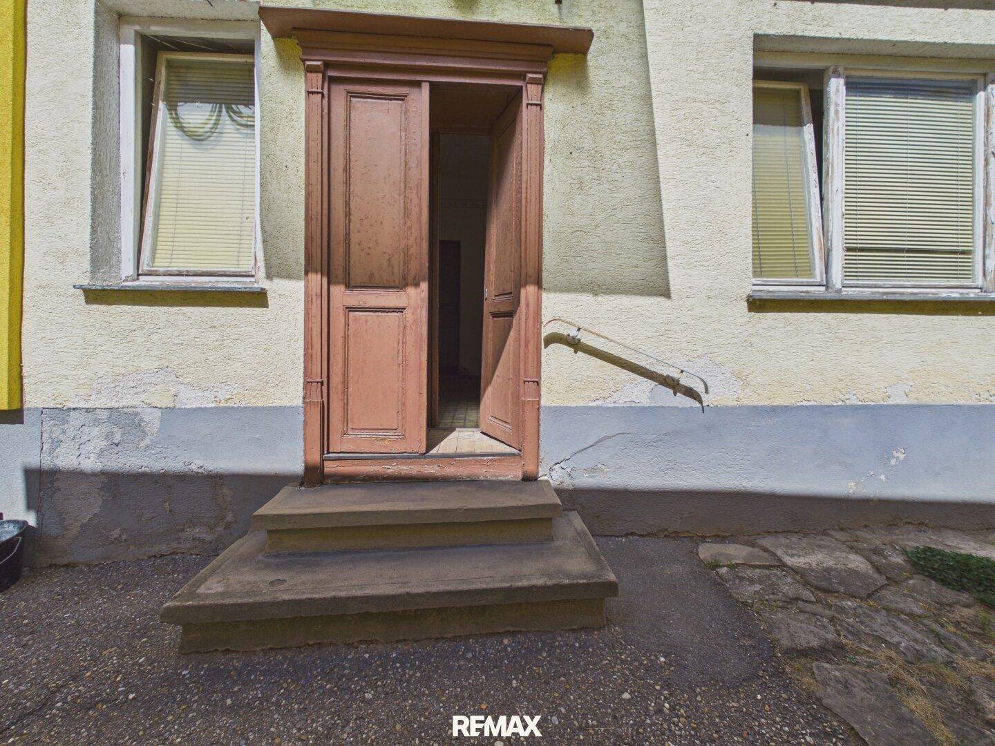 Detailansicht der alten Holztür mit Vordach und Stufen an der Hausfassade.