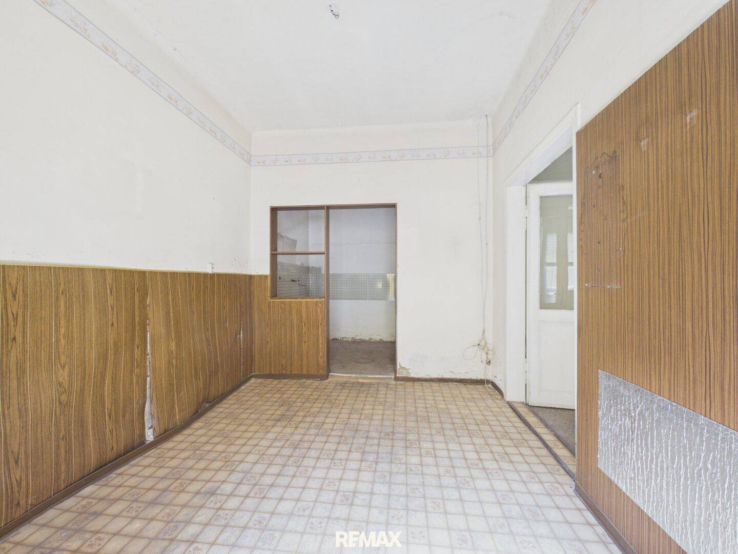 Renovierungsbedürftiger Innenraum mit Holzverkleidung und altem Vinylboden.