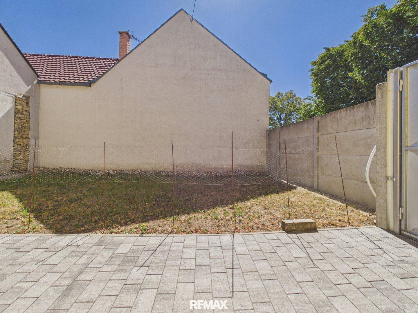 Gepflasterter Hofbereich mit Rasenfläche und hoher Mauer, sonniger Außenbereich.
