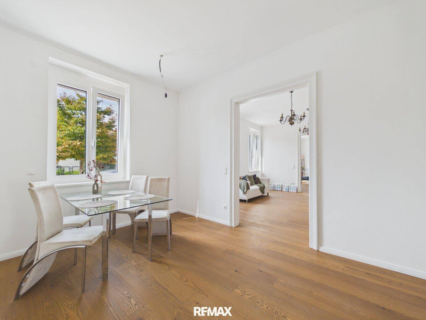 Heller Essbereich mit Glastisch und Stühlen, offen zum angrenzenden Wohnzimmer.