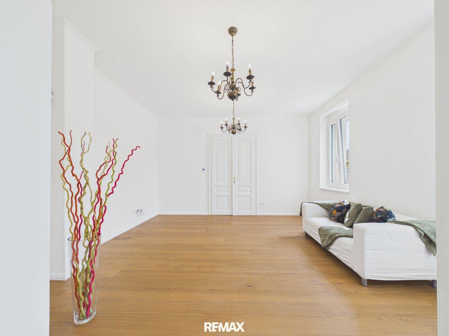 Geräumiges Wohnzimmer mit Holzboden, Kronleuchtern und einem Sofa.