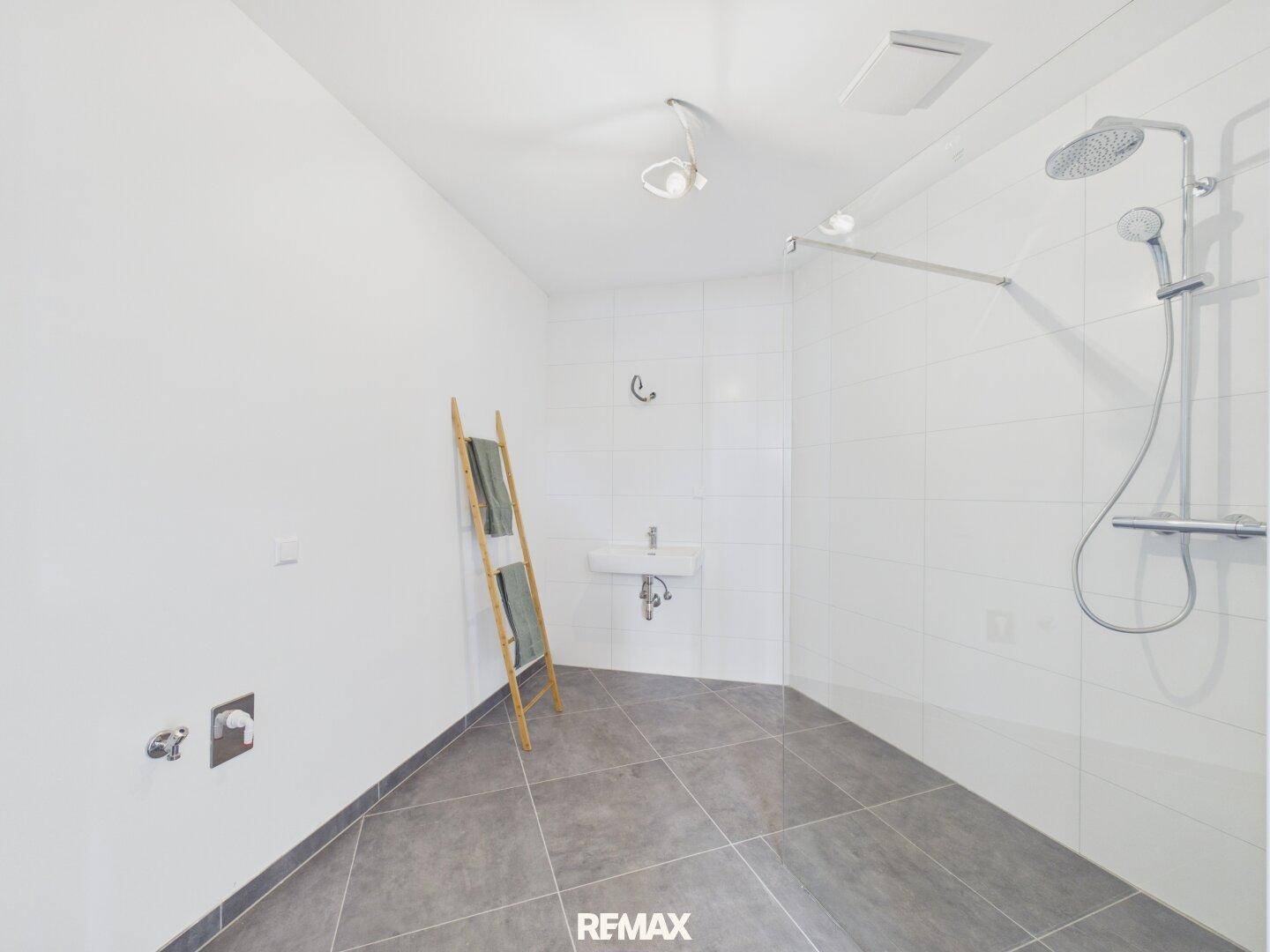 Modernes Badezimmer mit großer Dusche, Waschbecken und Anschluss für Waschmaschine.