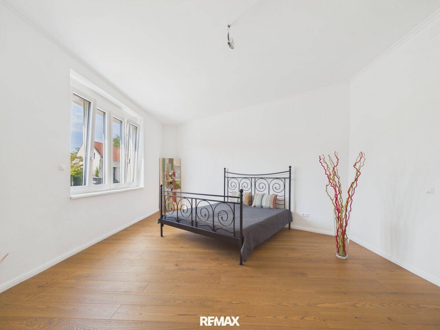 Helles Schlafzimmer mit Holzboden, großem Fenster und einem schmiedeeisernen Bett.
