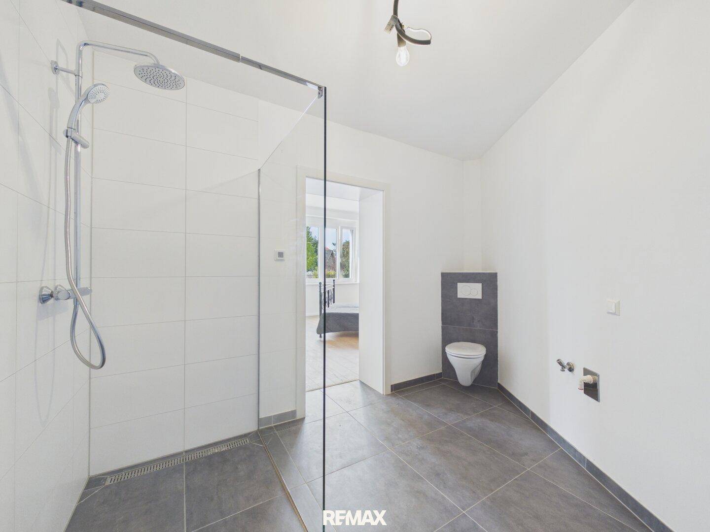 Geräumiges Badezimmer mit begehbarer Dusche und Wand-WC, mit Zugang zum Schlafzimmer.