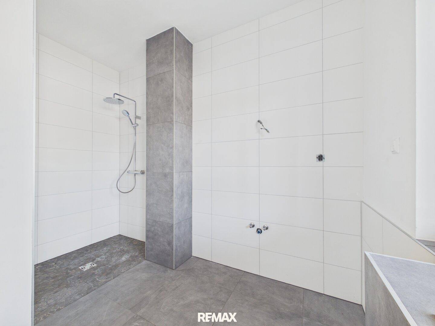 Modernes Badezimmer im Bau mit grauen Bodenfliesen und einer Duschkabine.