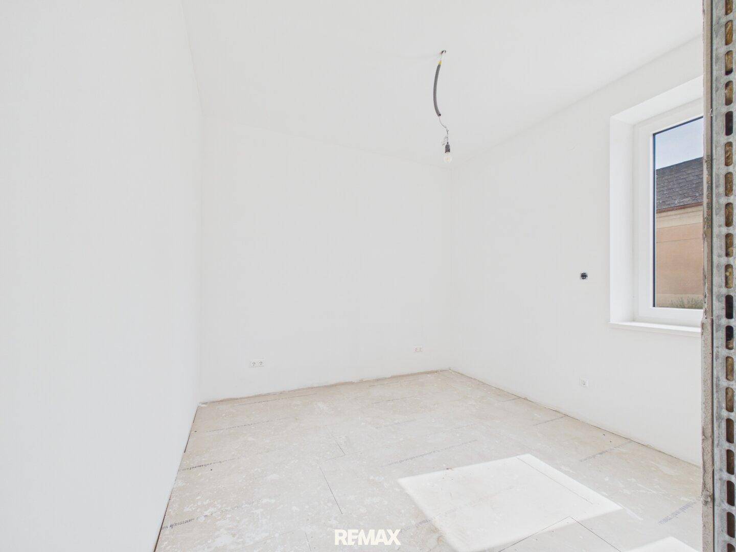 Helles Zimmer im Rohbau mit weiß gestrichenen Wänden und einem Fenster.