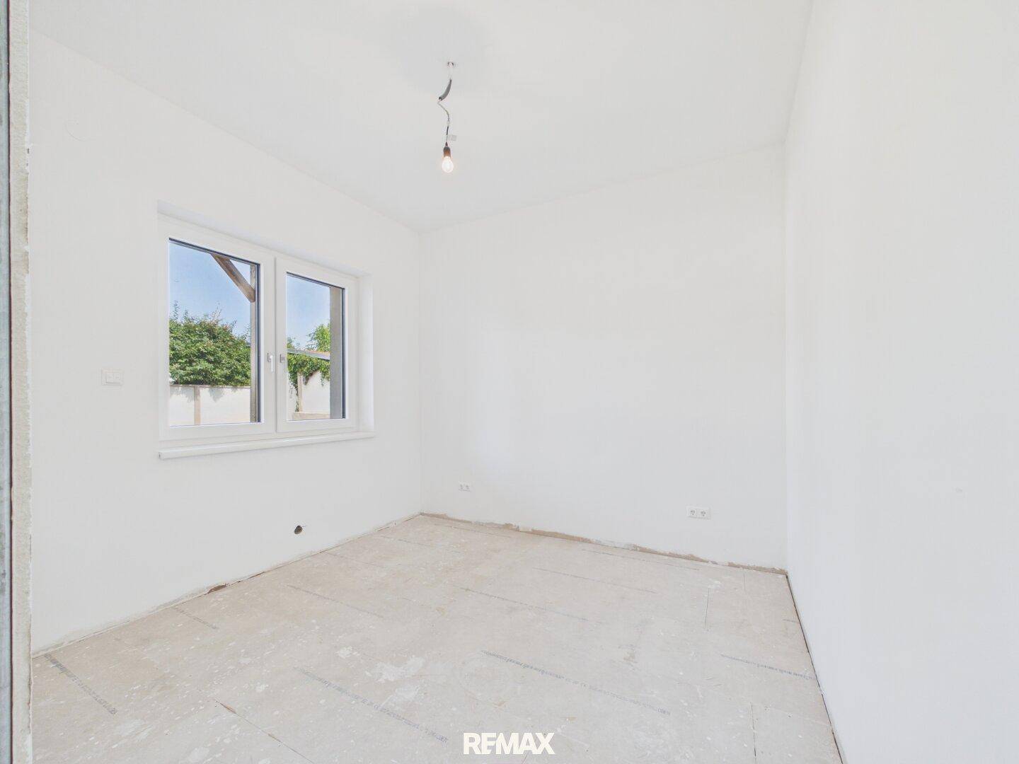 Helles Schlafzimmer im Rohbau mit Fenster und Blick ins Grüne.