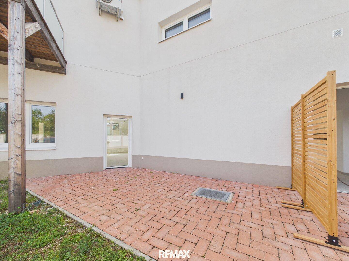 Gepflasterte Terrasse mit roten Ziegeln, Holzsichtschutz und Zugang zum Gebäude.