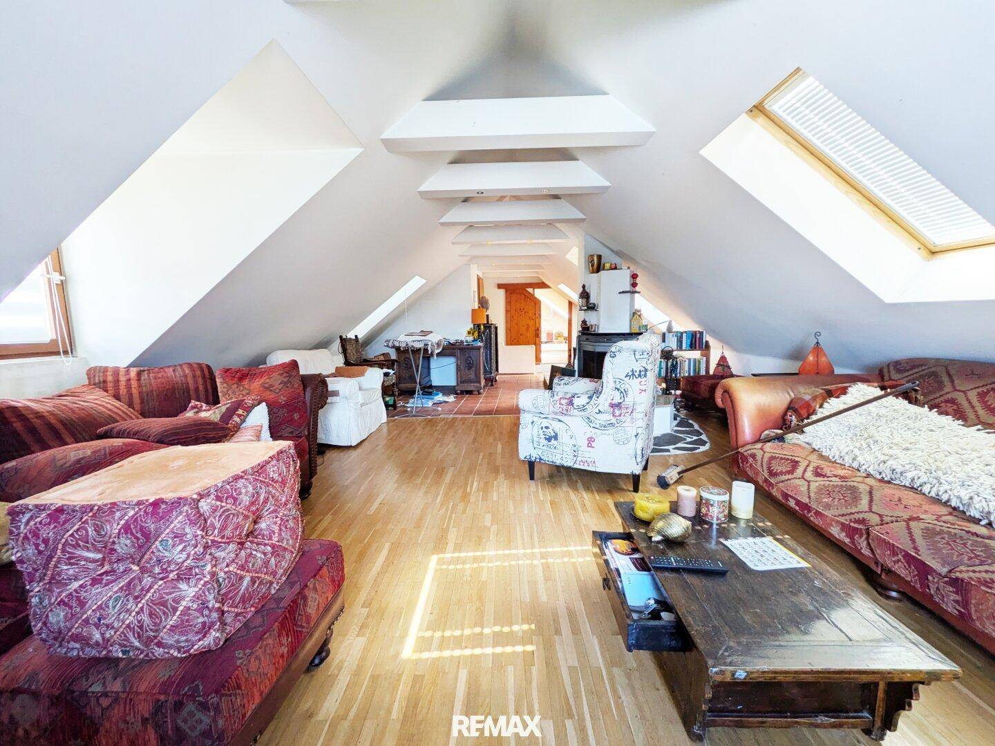 Helles Wohnzimmer im Dachgeschoss mit Holzboden, schrägen Decken und gemütlichen Sitzgelegenheiten.