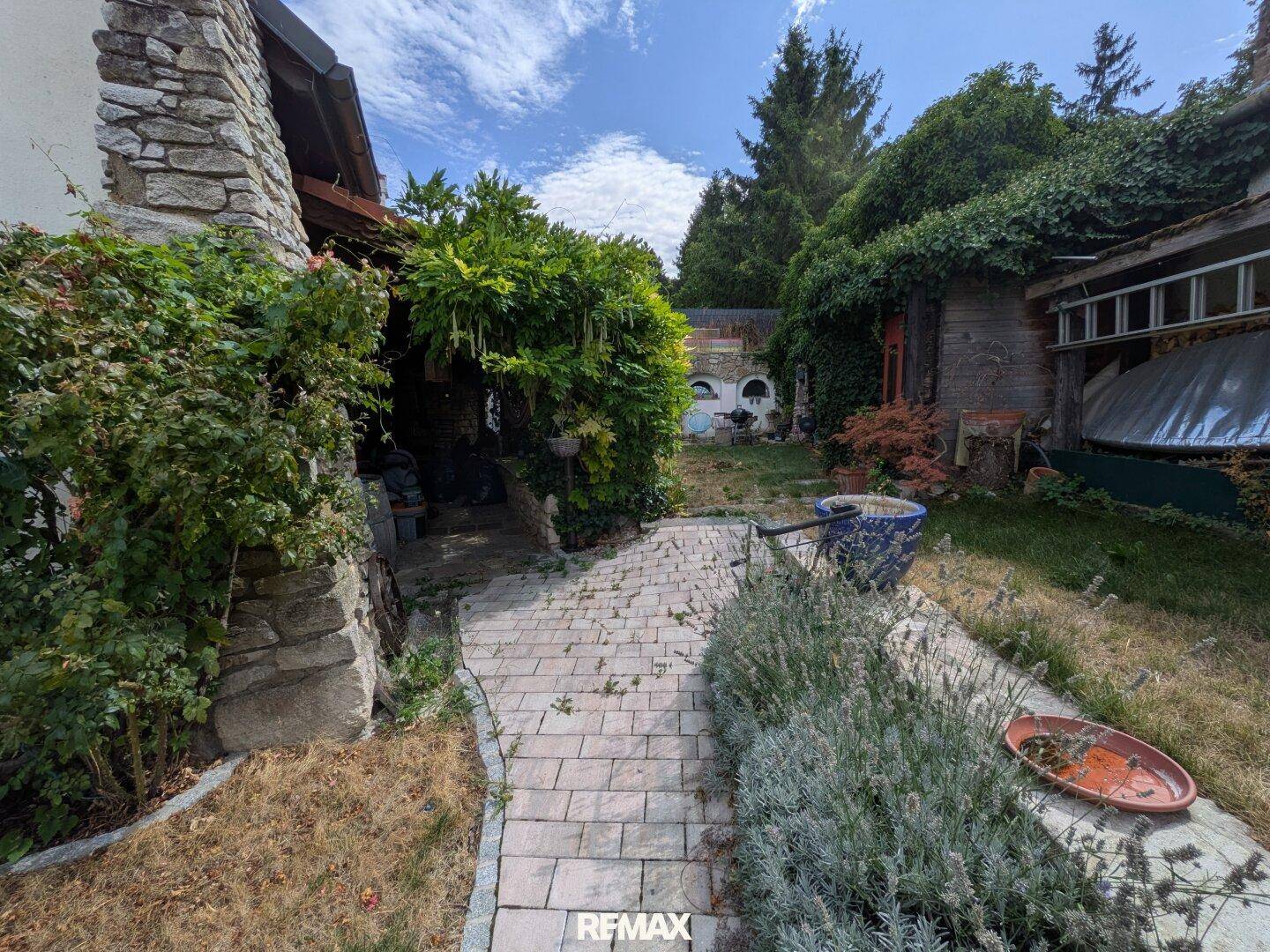 Steinweg führt durch einen üppig bewachsenen Gartenbereich mit Natursteinmauern.