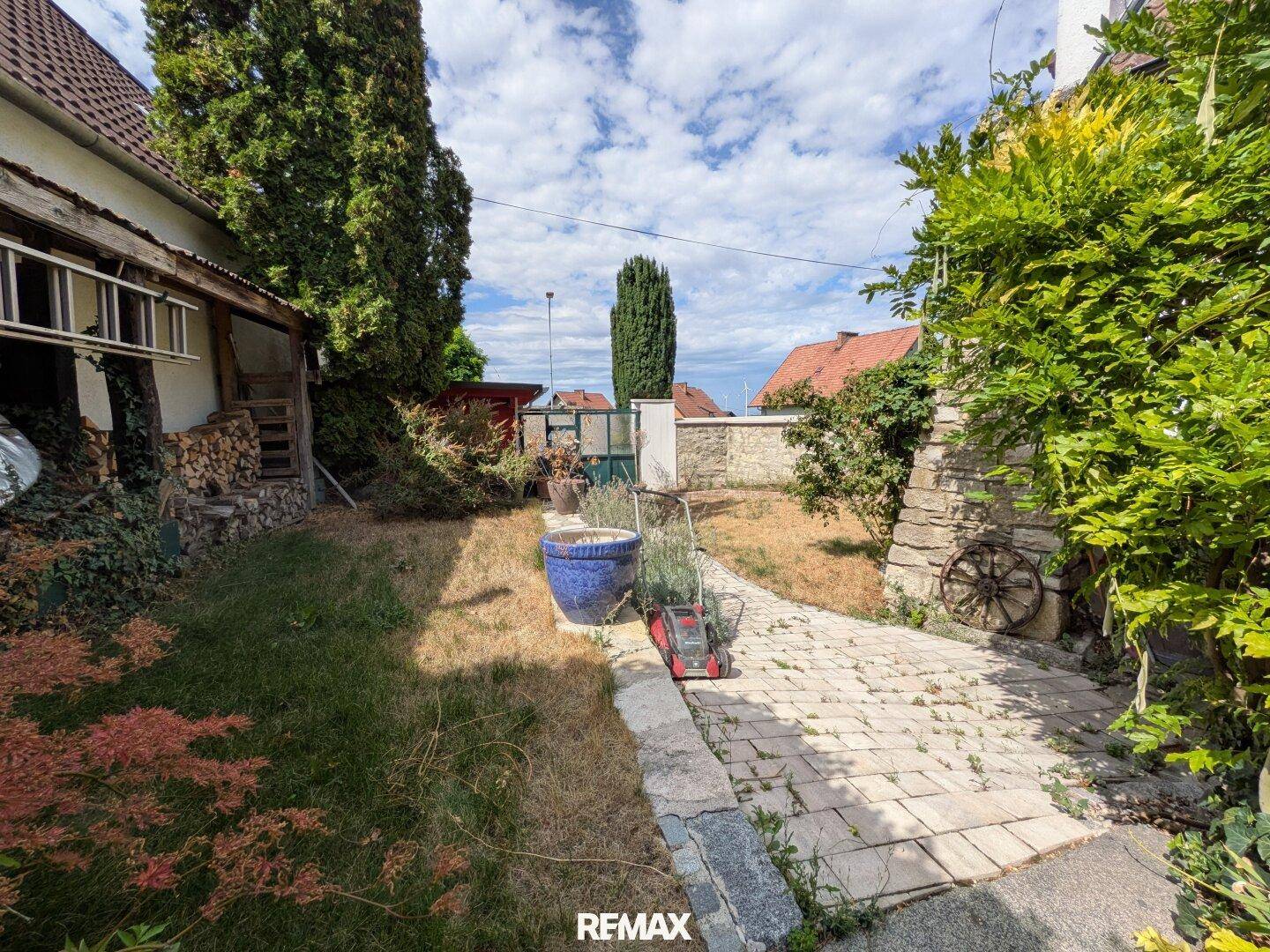 Gepflegter Gartenbereich mit Steinweg, Rasen und verschiedenen Pflanzen unter blauem Himmel.