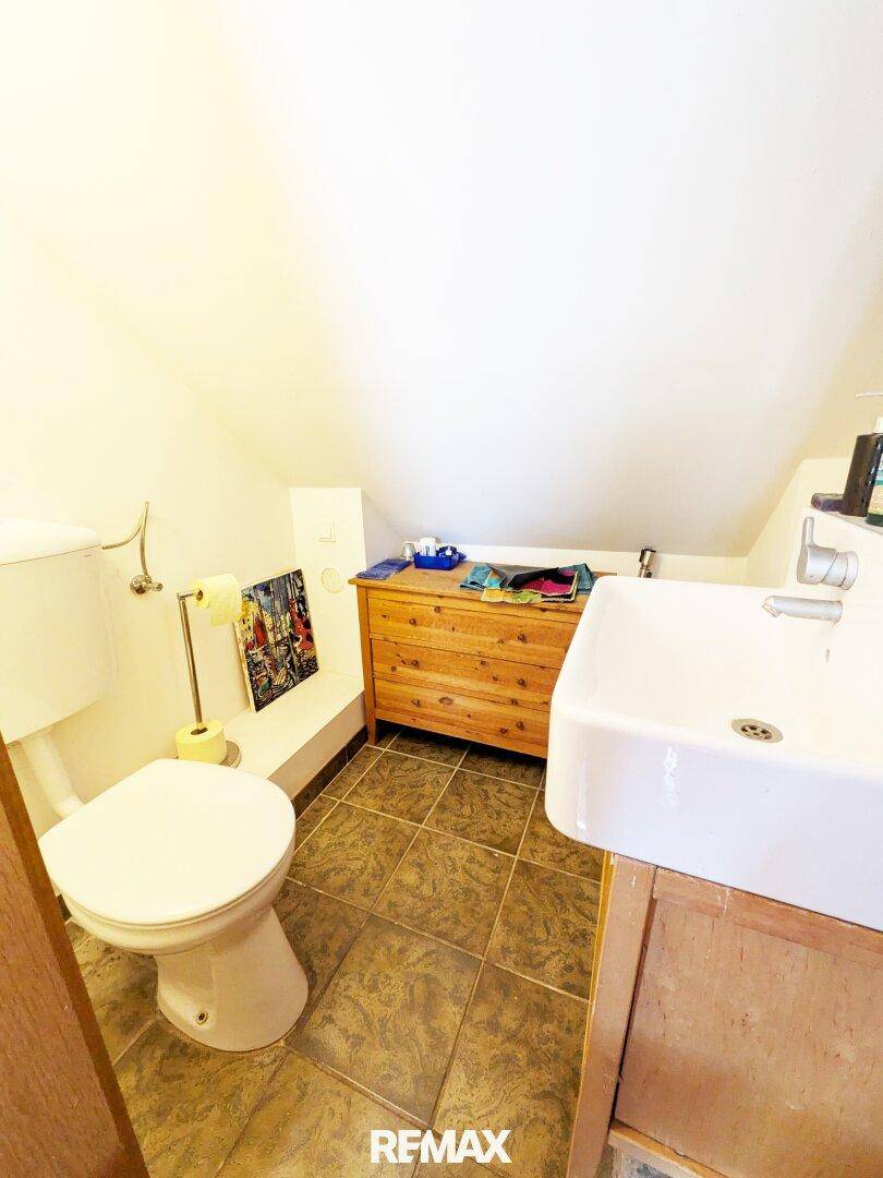 Kleines Gäste-WC mit dunklen Fliesen, Toilette und Waschbecken unter einer Dachschräge.
