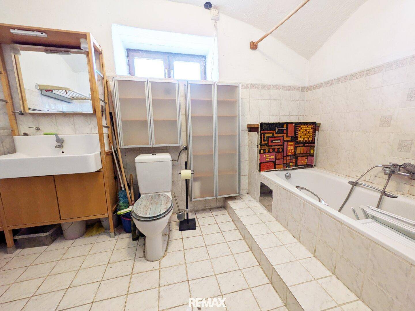 Badezimmer mit weißen Fliesen, Badewanne, Toilette und einem Fenster für Tageslicht.
