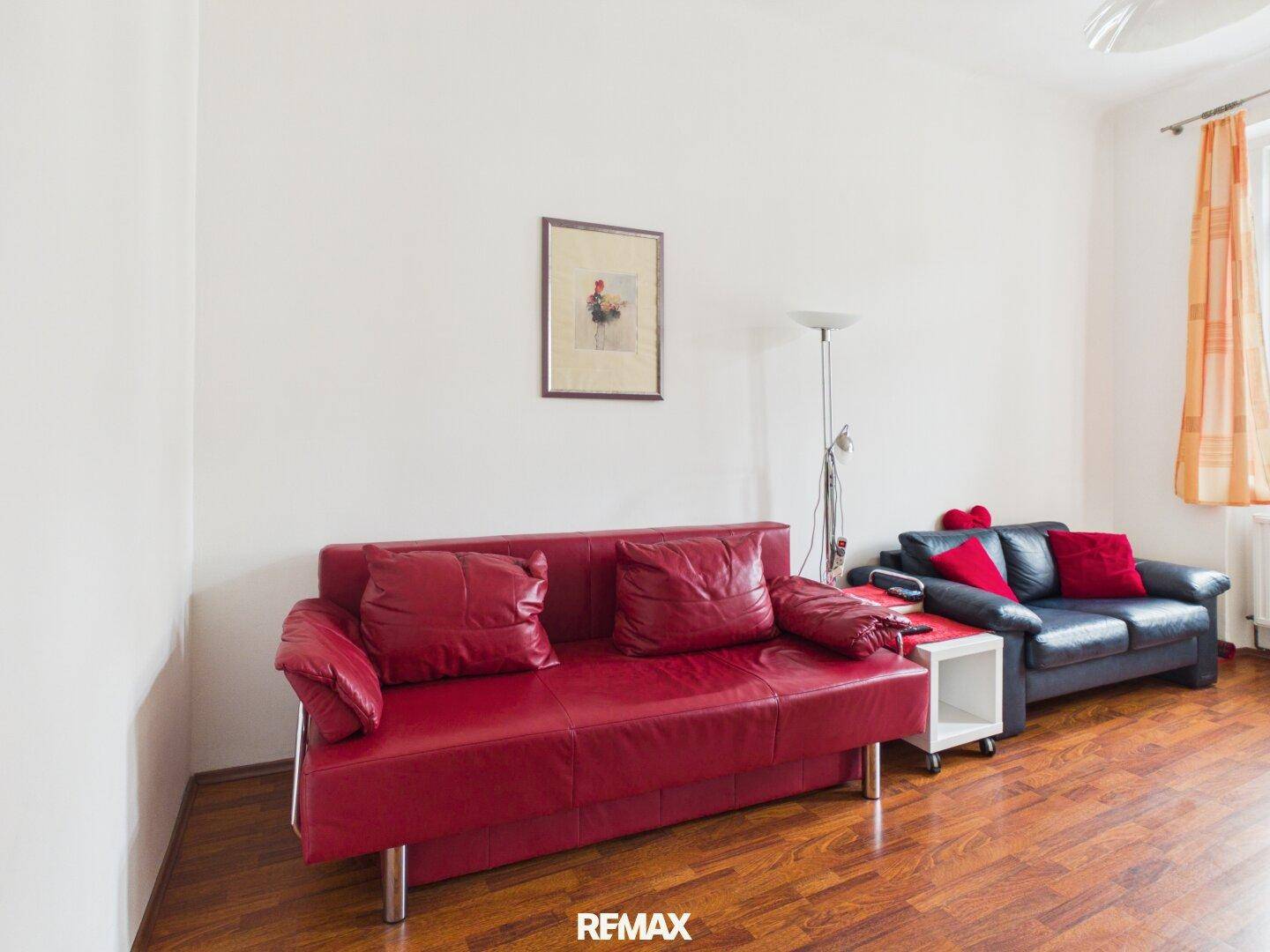 Gemütliches Wohnzimmer mit Holzboden und zwei Sofas in Rot und Dunkelblau für entspannte Stunden.