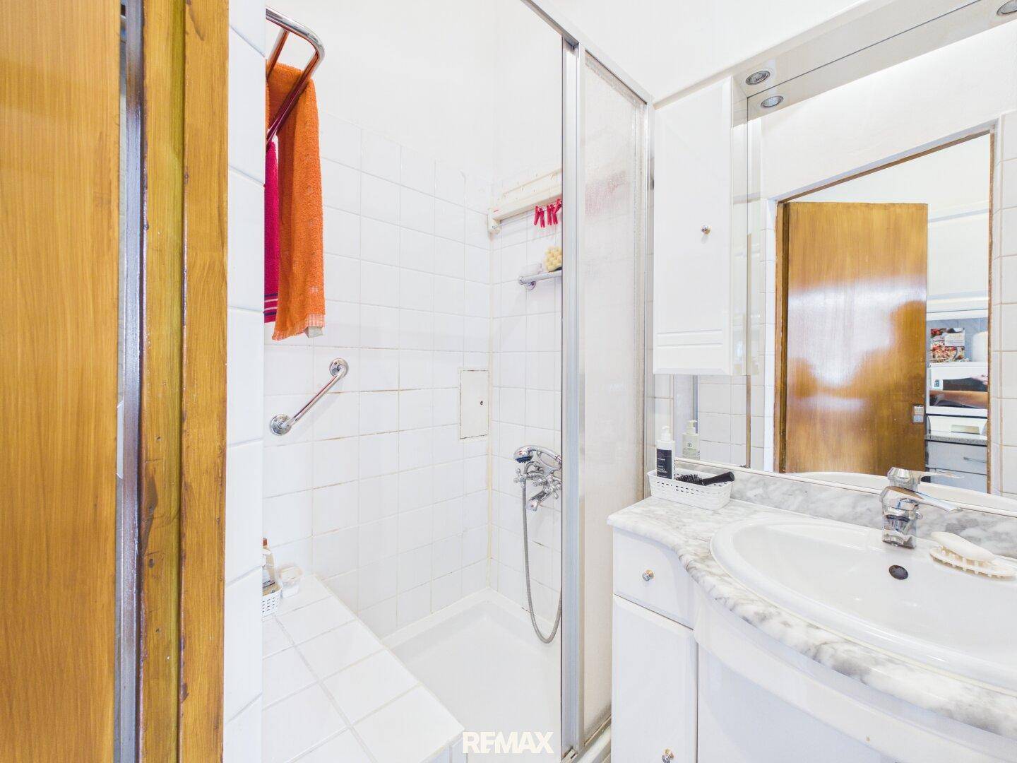 Badezimmer mit Duschkabine, Haltegriffen und weiß gefliesten Wänden für Sicherheit und Hygiene.