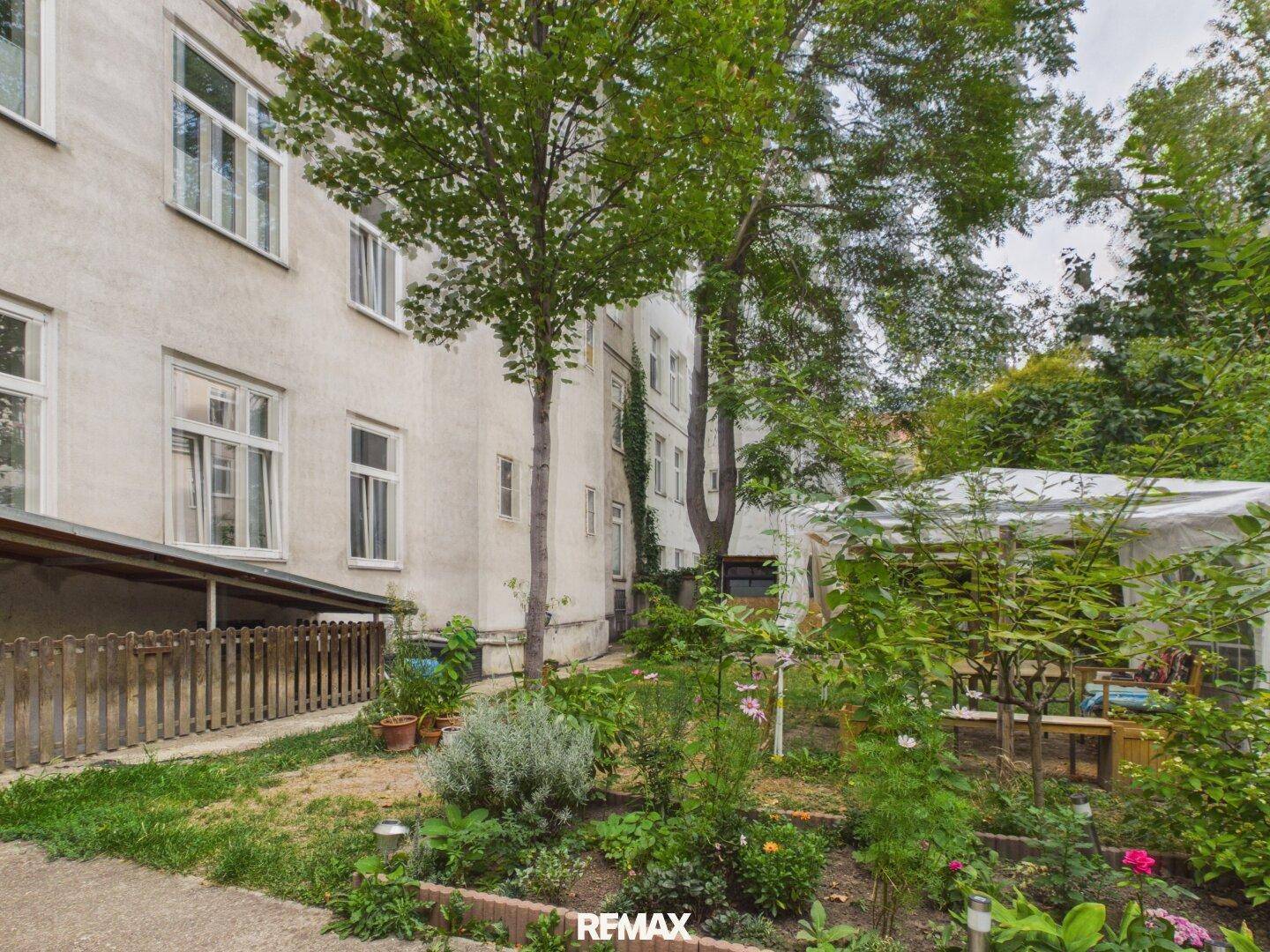 Grüner Hinterhofgarten mit Bäumen, Pflanzen und einem Pavillon im Hintergrund.