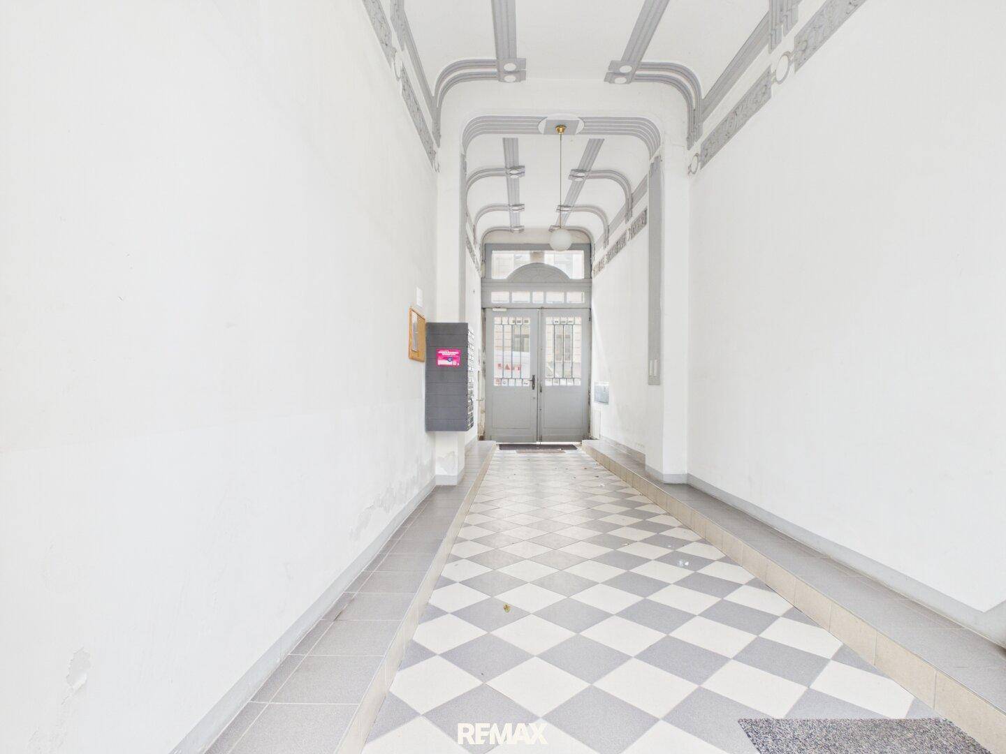 Langer, heller Eingangsbereich mit Schachbrettmuster-Fliesenboden und dekorativer Decke im Altbau-Stil.