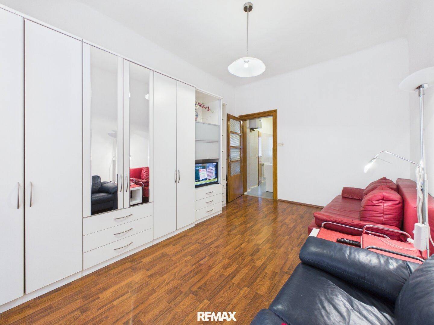 Wohnzimmer mit großer weißer Schrankwand, Spiegeltüren und Holzboden für viel Stauraum.