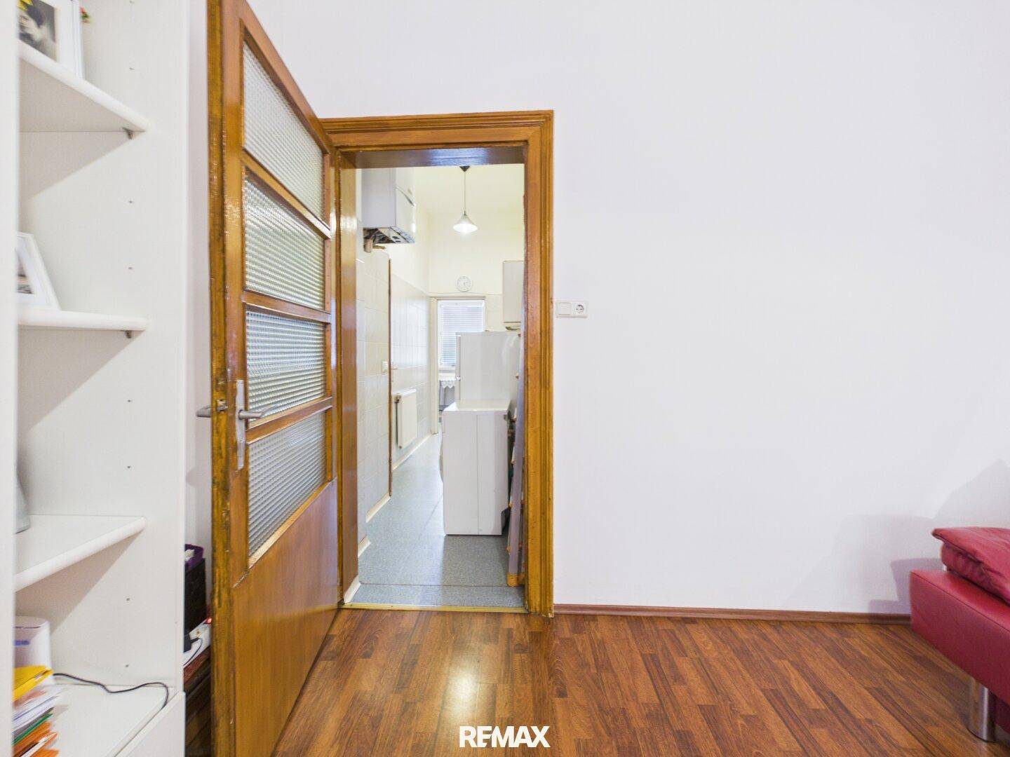 Blick vom Wohnzimmer durch eine Holztür in einen langen Flur mit Fliesenboden.