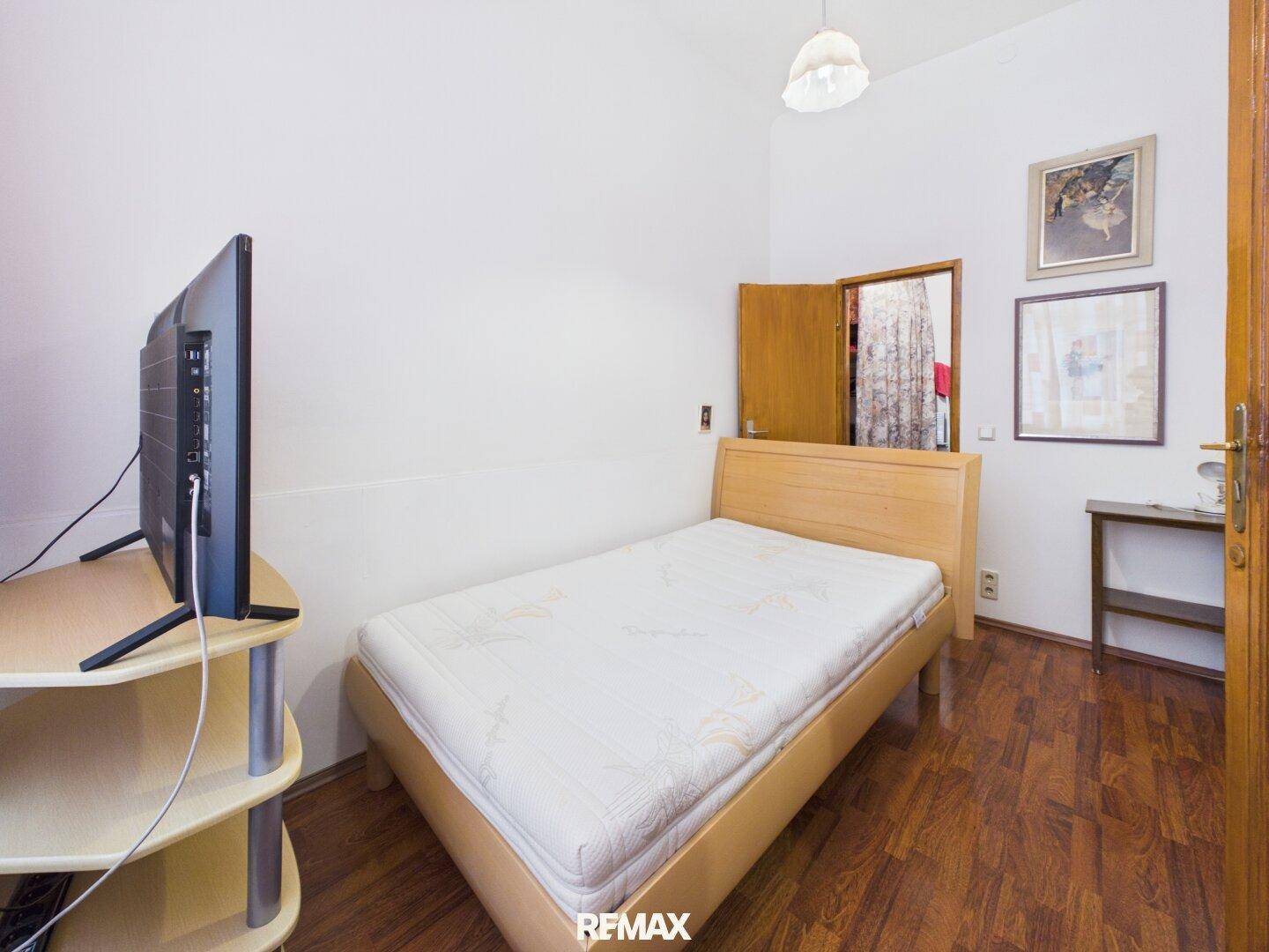 Schlafzimmer mit Holzbett, Fernseher und Holzboden, durch eine Tür sichtbar.