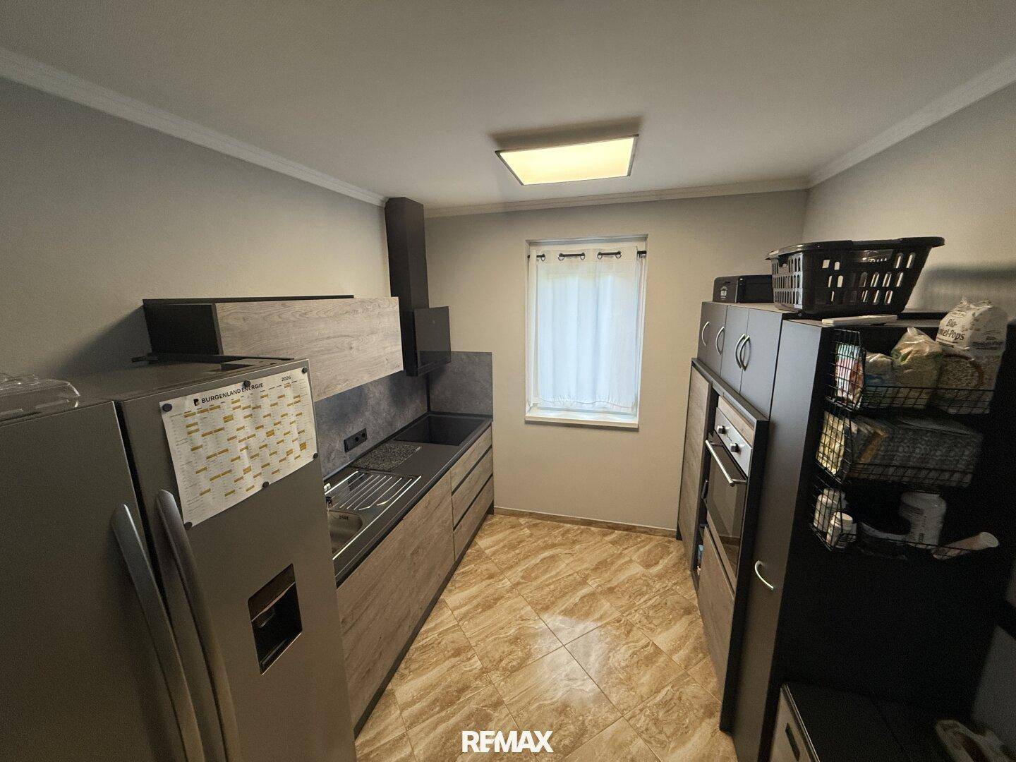 Moderne Küche mit Holzfronten, dunkler Arbeitsplatte, großem Kühlschrank und Fenster.