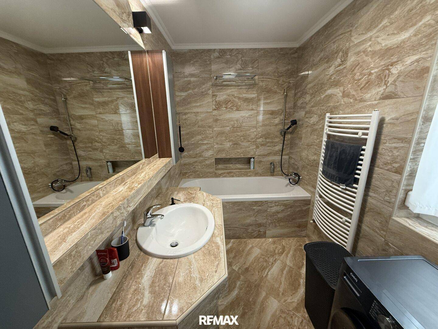 Gefliestes Badezimmer mit Badewanne, Einzelwaschbecken, beheiztem Handtuchhalter und Waschmaschine.