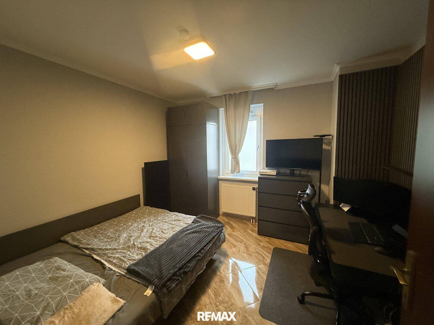 Schlafzimmer mit Bett, Schreibtisch, Fernseher und Fenster, ausgestattet mit Fliesenboden.