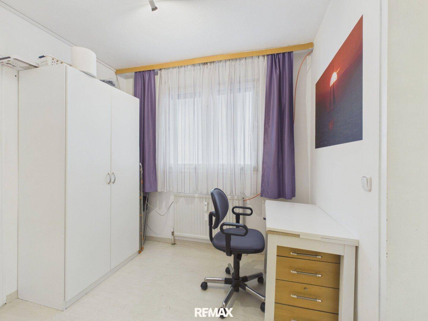 Kleines Büro oder Arbeitszimmer mit Schreibtisch, Stuhl und weißem Kleiderschrank.
