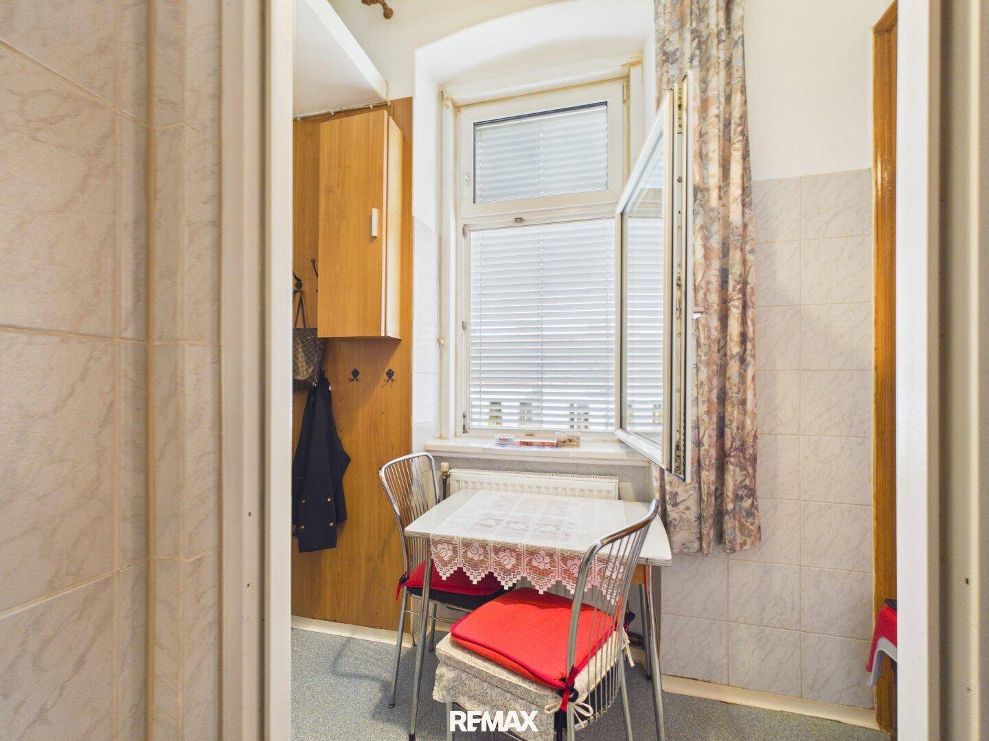 Kleine Küche mit Esstisch am Fenster, gefliesten Wänden und einfacher, funktionaler Einrichtung.