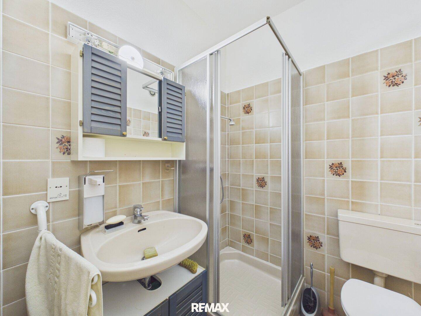 Gefliestes Badezimmer mit Dusche, Waschbecken und WC, in einem traditionellen Stil gehalten.