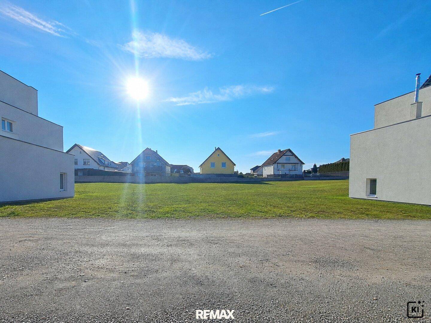 Großes grünes Grundstück unter blauem Himmel mit Sonnenschein, umgeben von modernen und traditionellen Häusern.
