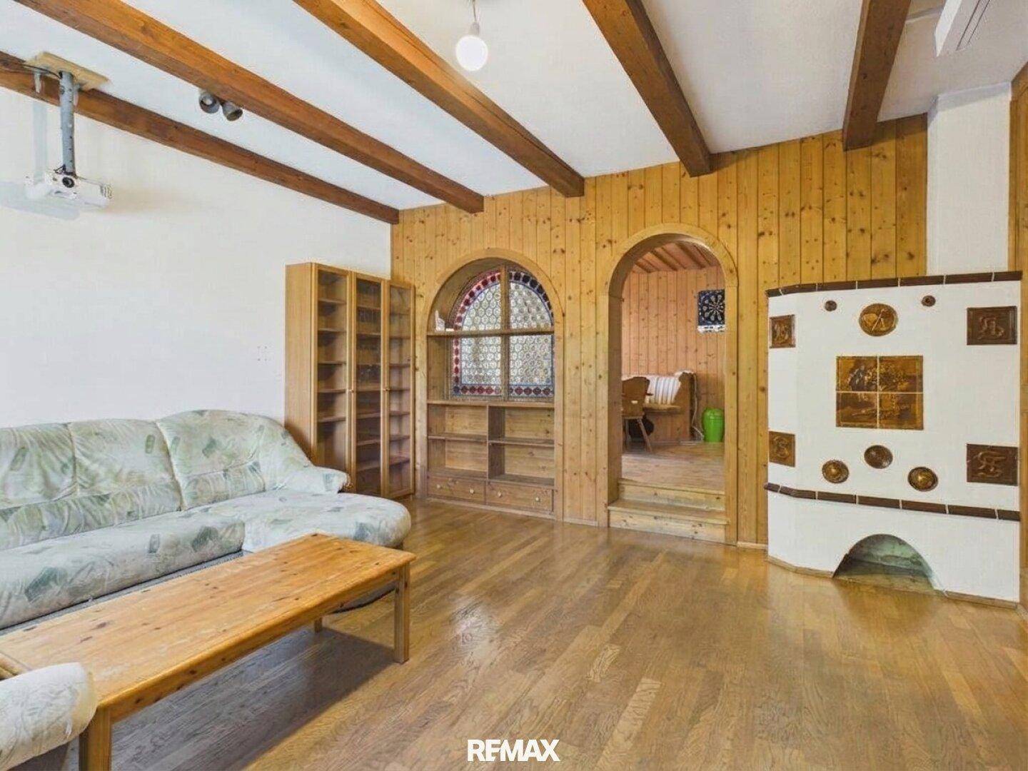 Rustikales Wohnzimmer mit Holzbalkendecke, Kachelofen und Holzboden.
