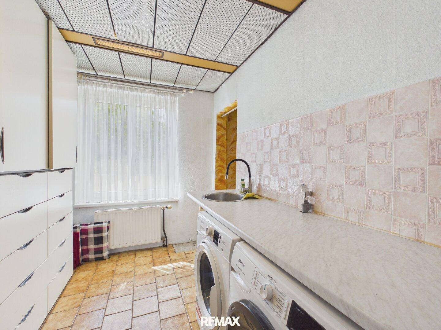 Waschküche mit Waschmaschine, Trockner und Spülbecken unter einem Fenster.