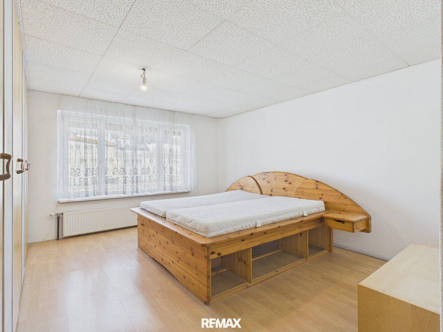 Schlafzimmer mit Holzbett, Parkettboden und großem Fenster.