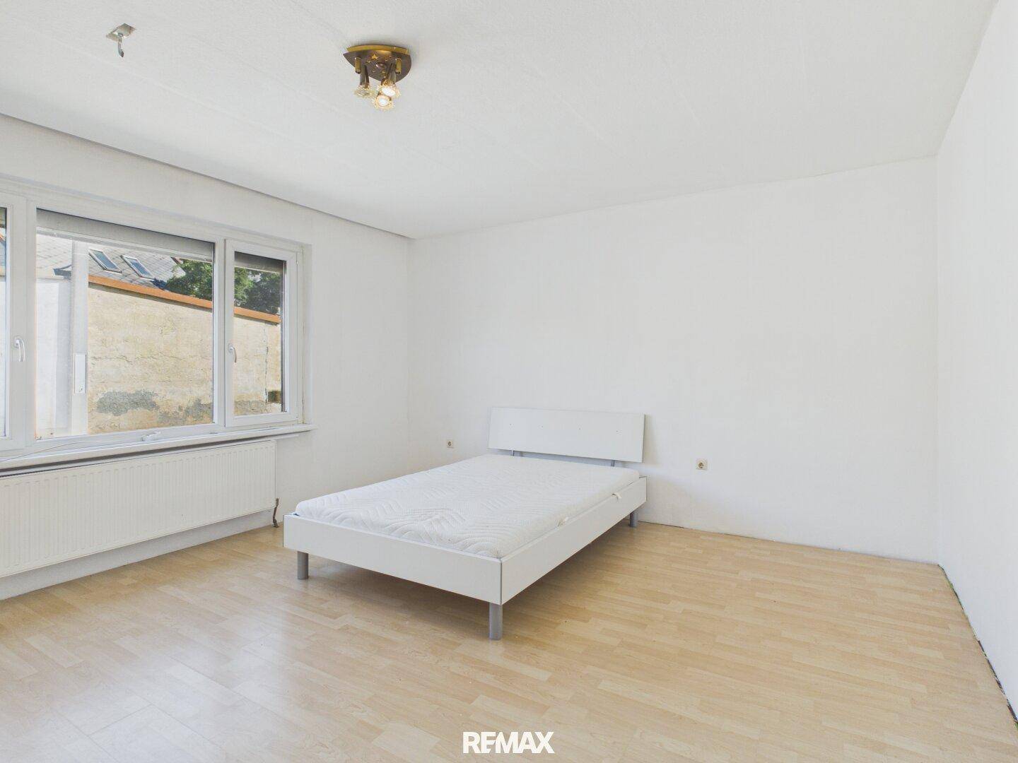 Helles Schlafzimmer mit Einzelbett, Parkettboden und Fensterblick nach draußen.