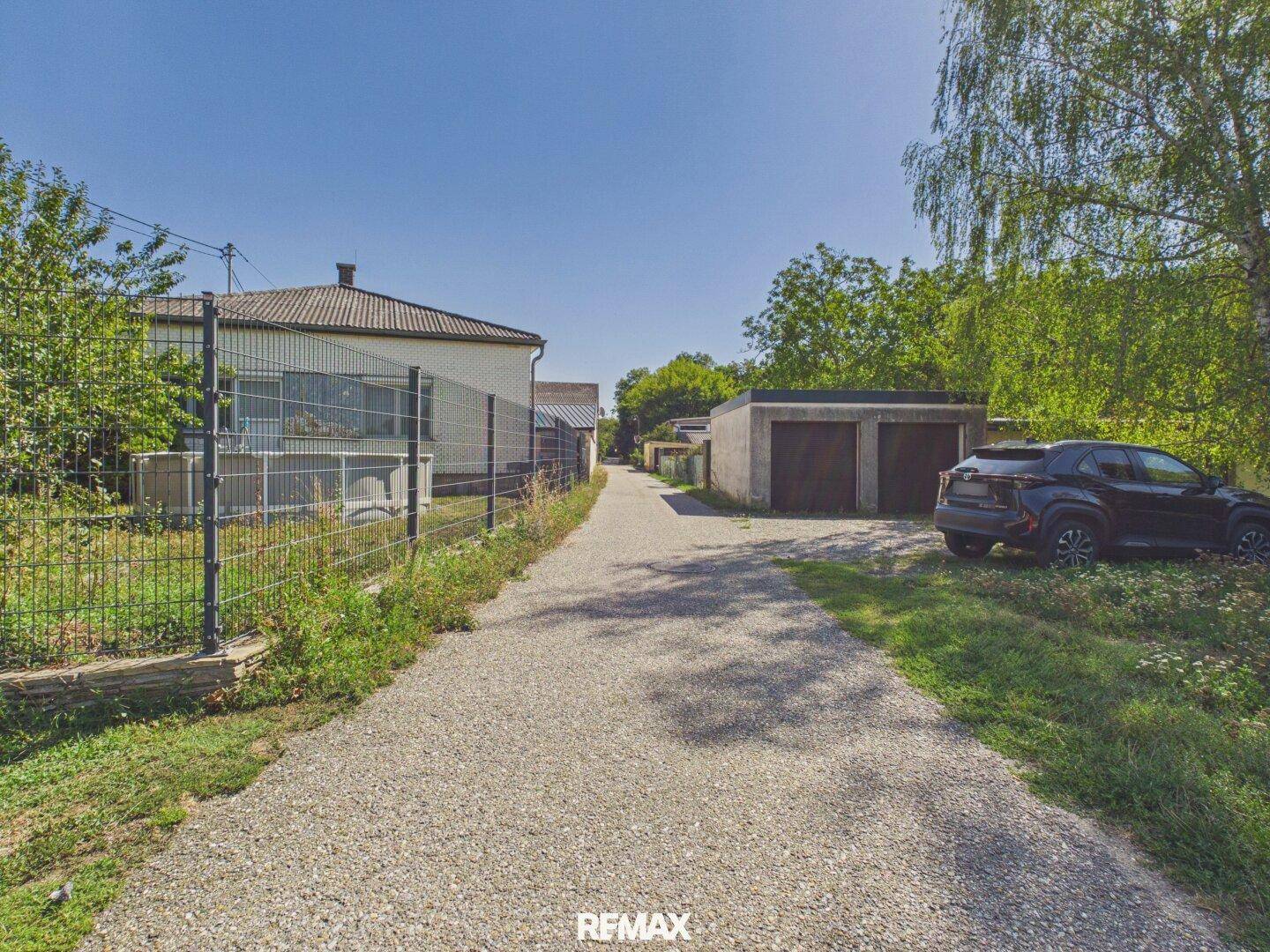 Kiesauffahrt führt zu zwei Garagen und dem Haus im Hintergrund.